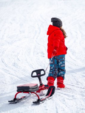 Kayak merkezinde zaman geçirirken kızak çeken ve karlı yamaçlarda koşan çocuğun arka görünümü