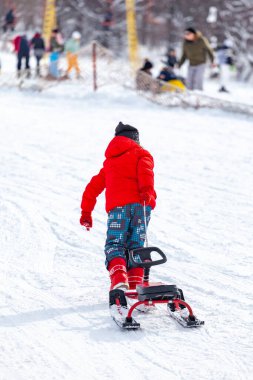 Kayak merkezinde zaman geçirirken kızak çeken ve karlı yamaçlarda koşan çocuğun arka görünümü