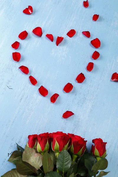 Serce czerwone płatki róż, niebieski płyty drewniane. — Zdjęcie stockowe