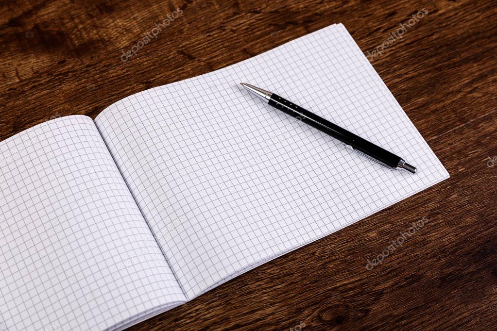 Notepad with pen on the wooden desk. Mockup.