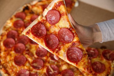 Biberli ya da salamlı pizza. Bir parça tutan el.