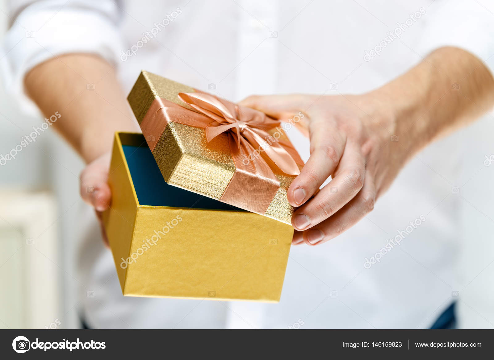 Male hands holding a t box Opened present wrapped with ribbon and bow Christmas or birthday golden paper package Man in white shirt