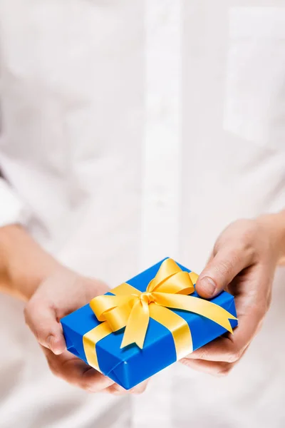 Manos masculinas sosteniendo una caja de regalo azul con cinta . — Foto de Stock