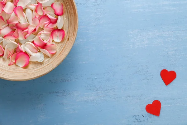Kırmızı kalp ve gül yaprakları mavi ahşap tahta üzerinde.
