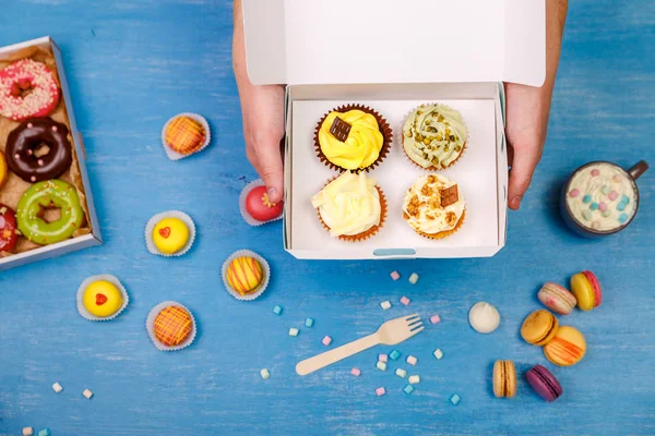 Cupcakes, donuts and macaroons. Hands holding.