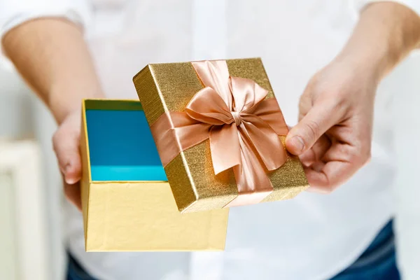 Male hands holding opened gift box with ribbon.