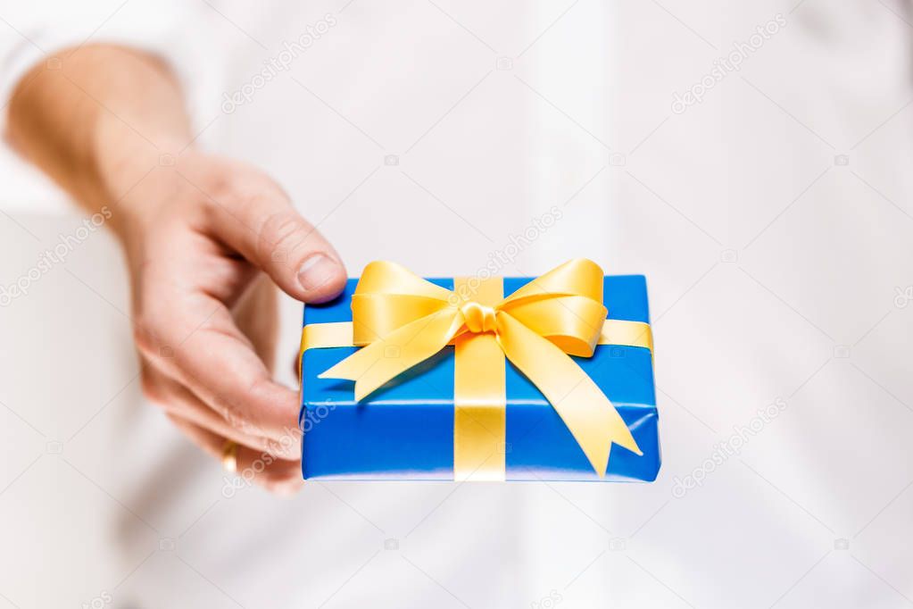 Male hand holding a blue gift box with ribbon.