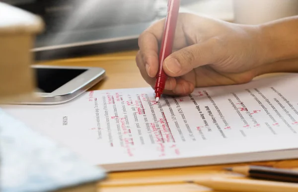 Mão segurando caneta vermelha sobre o texto de revisão — Fotografia de Stock