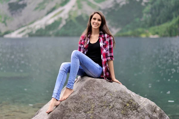 Una chica está sentada en una gran roca sobre el fondo de a la — Foto de Stock