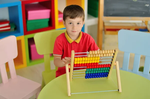 Um menino no quarto das crianças brincando na mesa com contas — Fotografia de Stock