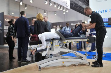 MEDICA Ticaret Fuarı, DÜKSELDORF, GERMANY - Kasım 2019, manuel terapi, bir eğitmen koltukta oturan bir kadının sırtını tedavi eder.