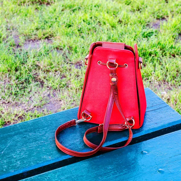 Zářivě Červená kabelka stojí na modré dřevěné lavice, opěradle — Stock fotografie