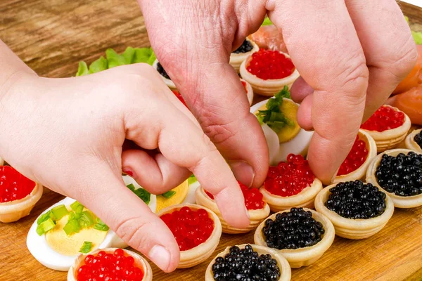 Mänskliga händer ta tartlets med röd och svart kaviar. Mat bakgr — Stockfoto