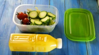 İnsan elleri taze salata, salatalık ve vişneli domatesle plastik beslenme çantasını doldurur. Yakında plastik bir şişe portakal suyu var. Sağlıklı vejetaryen gıda konsepti. Üst Manzara. Yakın plan..