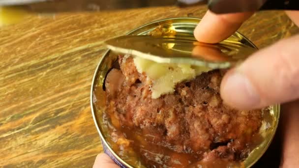 Canned meat. Human hands cut piece of stewed meat from a tin can using kitchen knife on wooden table. Close-up. — Stock Video
