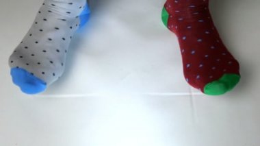 Farklı renkte çoraplar giyen insan bacakları beyaz katı yüzeyde hareket eder. Belki dans ediyordur, spor yapıyordur ya da spor yapıyordur. Yakın plan..