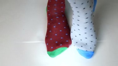 Farklı renkte çoraplar giyen insan bacakları beyaz katı yüzeyde hareket eder. Belki dans ediyordur, spor yapıyordur ya da spor yapıyordur. Yakın plan..