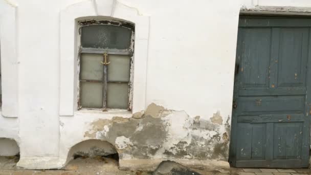 Zvětralá a poškozená zeď starého domu, omítnutá bílou od poškození a prasklin. A staré dřevěné dveře. Detailní záběr. — Stock video