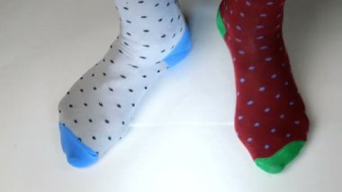 Farklı renkte, modaya uygun çoraplar giyen insan bacakları beyaz katı yüzeyde hareket eder, yürür ve tepinir. Belki dans ediyordur, spor yapıyordur ya da spor yapıyordur. Yakın plan..