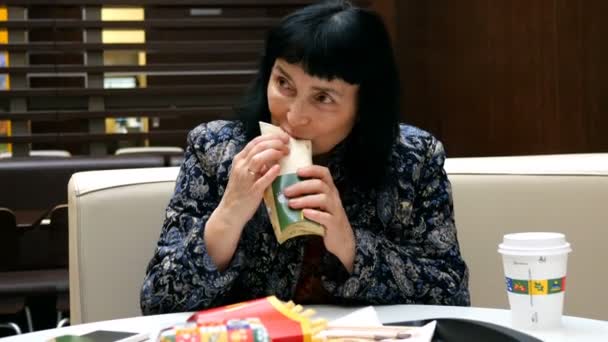 Kiev, Ukraina, Desember 2019: - Seorang wanita dewasa bergaya dari etnis Asia makan makanan cepat saji dengan senang hati dan minum kopi dari cangkir kertas di restoran mcdonald di Kiev . — Stok Video