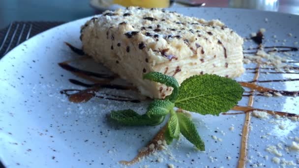 Smaklig efterrätt. Skiva av Napoleon gräddtårta, gjord av smördeg, ligger på en tallrik på ett bord i en restaurang eller café. — Stockvideo