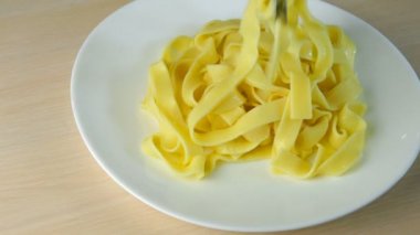 Lezzetli ev yapımı yemek. Makarna ya da spagetti, mutfak maşasıyla birlikte beyaz tabağa konur, güveç eklenir ve baharatlı mantar sosuna dökülür. Açık ahşap masada. Yakın plan..