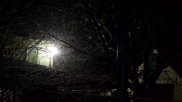 Снегопад на заднем дворе старого дома и свет фонаря ночью. Загадочный зимний сельский пейзаж. Средний план . — стоковое видео