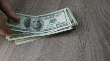 Eller ahşap masada yığınla dolar katlar. Bir banknottan diğerine. Belki de birikimlerini aktarıyordur ya da kar yapıyordur. Yakın plan..