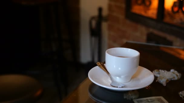 Kopp kaffe finns på bord i café eller restaurang med öppen spis. Brinnande flammor reflekterar på bordet. Romantisk miljö. Selektivt fokus. Medelstor plan. — Stockvideo