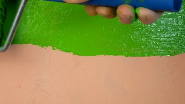 Рука человека окрашивает розовую стену в ярко-зеленый цвет с помощью ролика краски. Крупный план . — стоковое видео