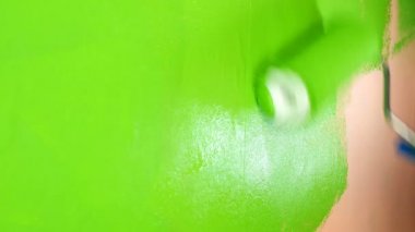 Human hand paints pink wall in bright green color with paint roller. Medium plan.