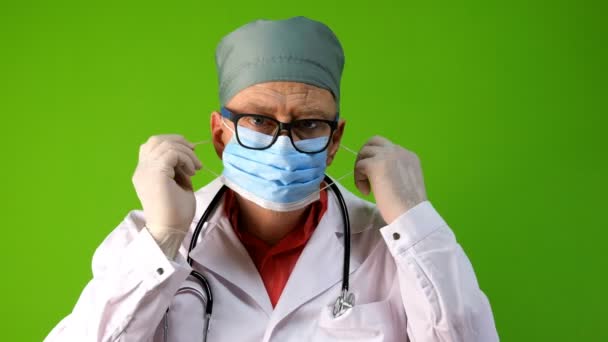 백인 국적을 가진 노인 의사는 흰 코트를 입고 냅킨 뒤에 숨어서 의료용 마스크와 기침을 한다. 코로나 바이러스 치료중 감염의 위험성에 대한 개념이다. 클로즈업. — 비디오