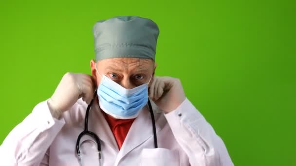 Tıbbi maskeli kıdemli yetişkin doktor ve şırıngayla tıbbi eldiven enjeksiyona hazırlanıyor. Virüs koruma aşısı konsepti. Yeşil arka planda. Krom anahtar. Yakın plan.. — Stok video