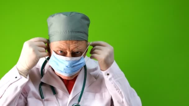 Tıbbi maskeli kıdemli yetişkin doktor ve şırıngayla tıbbi eldiven enjeksiyona hazırlanıyor. Virüs koruma aşısı konsepti. Yeşil arka planda. Krom anahtar. Yakın plan.. — Stok video