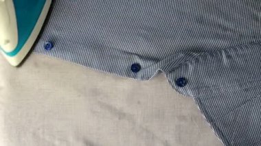 İnsan eli elektrikli ütüyle hafif tekstil zemininde mavi gömleği ütülüyor. Üst Manzara. Ev işi konsepti. Yakın plan..