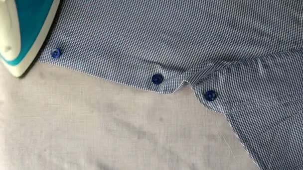 Human hand with electric iron is ironing blue shirt, on light textile background. Top view. Housework concept. Close-up. — Stock Footage Human hand with electric iron is ironing blue shirt, on light textile background. Top view. Housework concept. Close-up. Video Clip