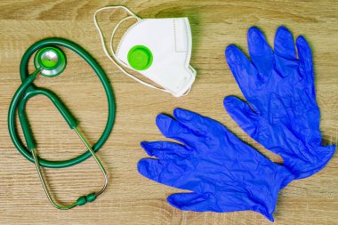 Solunum maskesi, yeşil steteskop ve plastik tıbbi eldiven, ahşap masada yatıyor. Tıp ve sağlık hizmetleri kavramı. Uzayı metin için kopyala. Üst Manzara. Yakın plan. Kapalı.