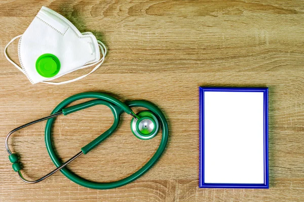 Respiratory mask, green stethoscope and blue blank frame, lie on wooden table. Concept of medicine and healthcare. Copy space for text. Top view. Close-up. Indoors.