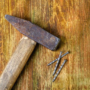 Eski paslı çekiç ve üç çelik çivi çizik ahşap bir masada yatıyor. Uzayı metin için kopyala. Seçici odaklanma. Ev ödevi konsepti. Kare biçiminde. Üst Manzara. Yakın plan..