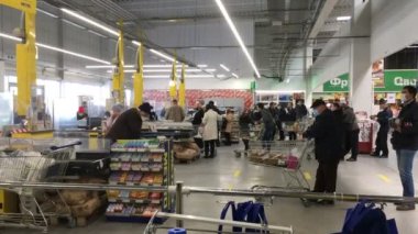 Kiev, Ukrayna, Mart 2020: Coronavirus covid-19 salgını sırasında alışveriş arabalarıyla tıbbi maskeli alıcılar süpermarketteki kasada ya da mağazada sıraya giriyorlar. Genel plan.