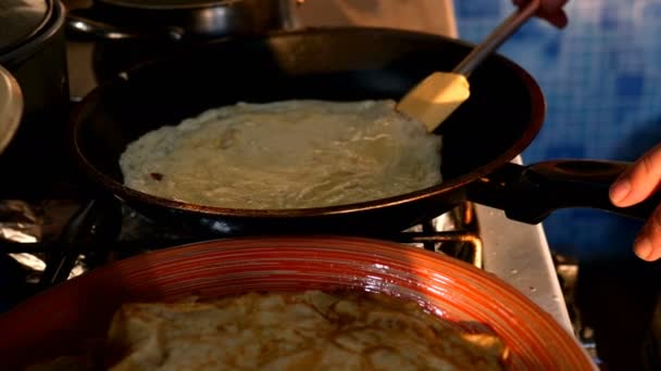 Vrouwelijke handen bakken pannenkoeken in koekenpan en draaien ze, op fornuis thuis in de keuken. Middelgroot plan. — Stockvideo