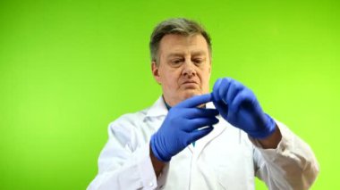 Beyaz önlüklü ciddi bir yetişkin doktor dışarıda enfeksiyon koruması için lastik eldivenlerini çıkarıyor. Yeşil arka plan. Kromakey. Yakın plan..