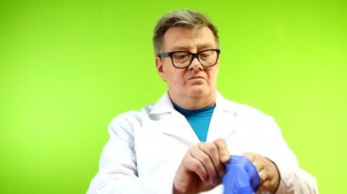 Beyaz önlüklü ciddi kıdemli doktor dışarıda enfeksiyonu koruyan koruyucu lastik eldivenlerini giydi. Yeşil arka plan. Kromakey. Yakın plan..