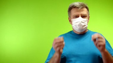 Pozitif kıdemli yetişkin adam dışarıda koronavirüsü koruyan koruyucu maskesini çıkarır ve göz kırpar. İyimserlik ve yaşam sevgisi. Yeşil arka plan. Kromakey. Yakın plan..