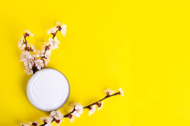 Kavanozda kozmetik kremi ve parlak sarı arka planda pembe çiçekli çiçek dalları. Doğal kremlerle cilt bakımı konsepti. Üst Manzara. Düz yatıyordu. Uzayı kopyala Soyut arkaplan.