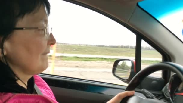 Oudere volwassen vrouw met een bril, rijdt met haar auto op de weg. Close-up portret. — Stockvideo