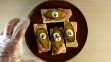 İnsanlar masada duran yuvarlak bir tabaktan sosisli ve salatalıklı sandviçleri alıyorlar. Yukarıdan aşağıya yemek..