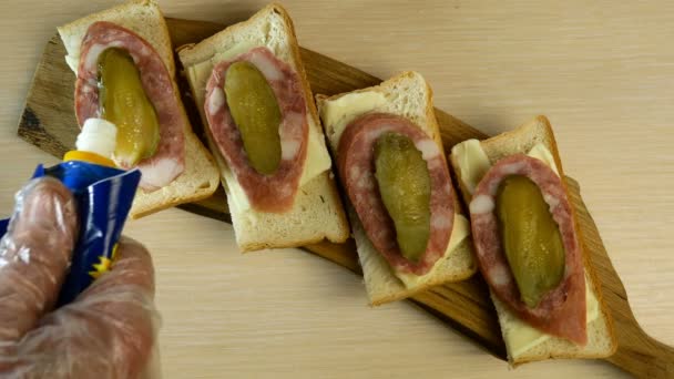 Human hand decorated sandwiches with sausage and pickled cucumber with drops of mayonnaise. On wooden cutting board. Top down food. — Stock Video