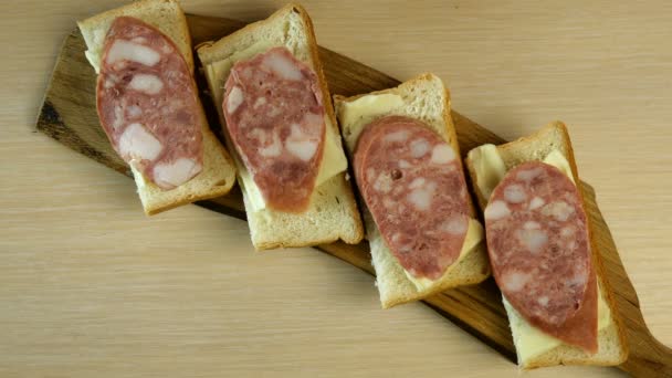 Человеческая рука кладет нарезанный маринованный огурец на колбасные сэндвичи, которые стоят на столе на разделочной доске. Сверху вниз . — стоковое видео