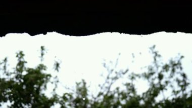 Yağmurlu bir gün. Kırsal kesimde ya da kır evindeki evin çatısından damlayan saydam yağmur damlacıkları. Ortalama bir plan. Açık havada..